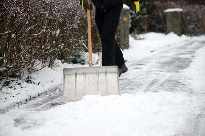 Mit einem Schneeschieber wird ein verschneiter Fußweg geräumt