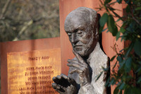 Büste aus Metall mit dem Gesicht und Händen von Kurt Masur an seinem Grabmal. Dahinter Teile eines Zitates von Franz von Assisi. 