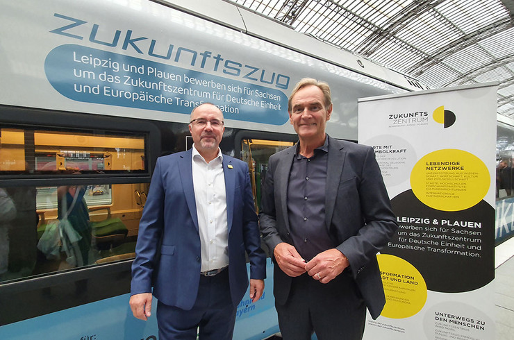 Plauens Oberbürgermeister Steffen Zenner und Leipzigs Oberbürgermeister im Anzug stehen vor einem blauen Zug