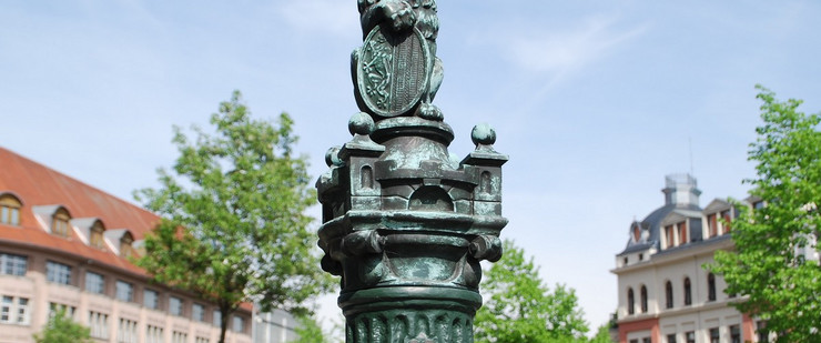 Metallskulptur eines Leipziger Löwen mit Stadtwappen auf einer Säule am Listplatz.