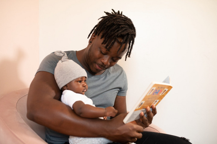 Ein Mann hat ein Baby auf dem Schoß und schaut mit ihm ein Bilderbuch an.