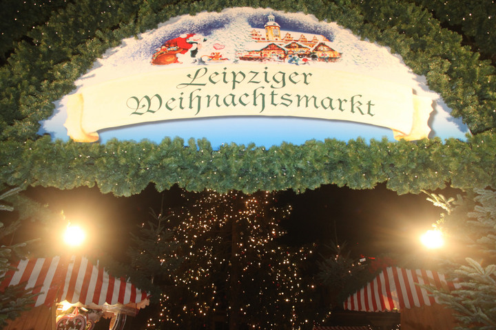 Großes Eingangsschild zum Weihnachtsmarkt mit dem Schriftzug: Leipziger Weihnachtsmarkt. Über der Schrift ist ein weihnachtliches Bild. Um das Schild sind Tannenzweige.