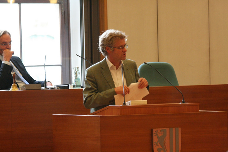 Ein Mann in Hemd und Jacket steht am Rednerpult und spricht. Him Hintergrund zu erkennen: Oberbürgermeister Burkhard Jung.