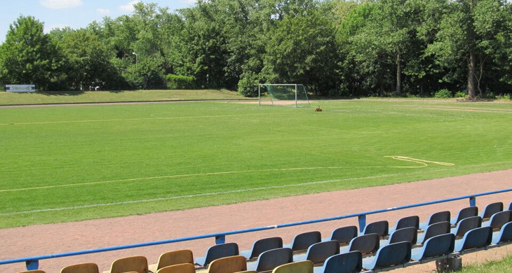 Fußballspielfeld mit drei Reihen Hartplastiksitzreihen davor.
