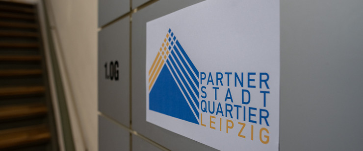 Nahaufnahme eines Etagenwegweisers mit Abbild des gelb-blauen Logos des Partnerstadtquartiers