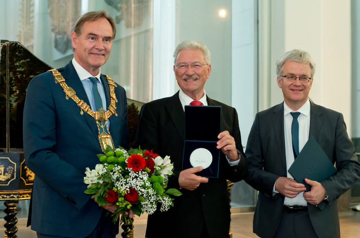 Klaus Mertens hält die Bachmedaille in seinen Händen, Oberbürgermeister Burkhard Jung steht mit einem Strauß Blumen neben ihm.
