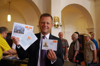 Bürgermeister Torsten Bonew hält die ersten gestempelten Briefmarken in die Kamera