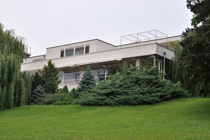 Eine weiße Villa im Bauhaus-Stil umgeben von einer grünen Wiese und grünen Bäumen.