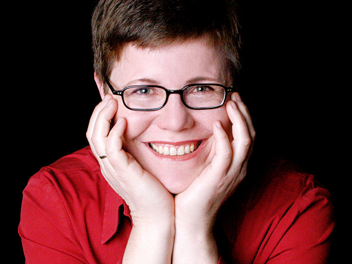 Eine Frau mit kurzen braunen Haaren und rotem Pullover und Brille lächelt ins Bild.