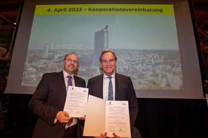Die Oberbürgermeister der Städte Plauen und Leipzig stehen vor einer Präsentationswand und halten Urkunden in den Händen.