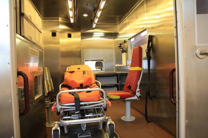 Blick in den Innenraum eines Infektions-Transportwagens. Darin befinden sich zwei Sitzplätze und eine Liege. Die Wände sind mit Edelstahl ausgekleidet.