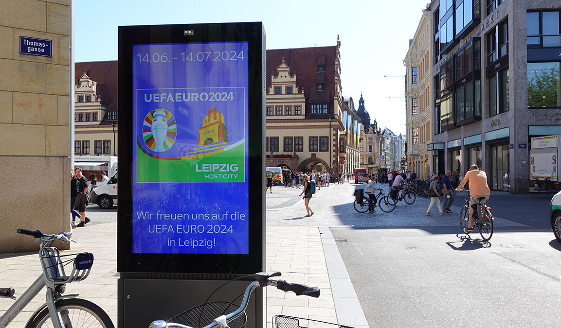 Digitale Anzeigentafel in der Leipziger Fußgängerzone am Markt mit dem Plakat zur UEFA EURO 2024. Mit dem Text "Wir freuen uns auf die UEFA EURO 2024 in Leipzig!"