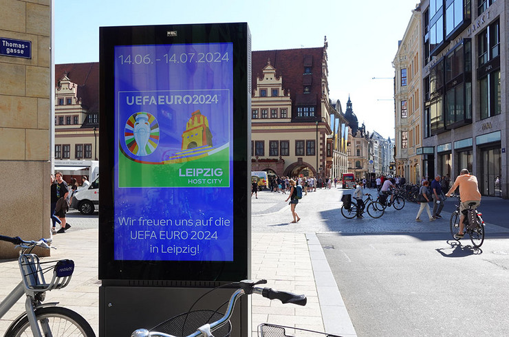 Digitale Anzeigentafel in der Leipziger Fußgängerzone am Markt mit dem Plakat zur UEFA EURO 2024. Mit dem Text "Wir freuen uns auf die UEFA EURO 2024 in Leipzig!"
