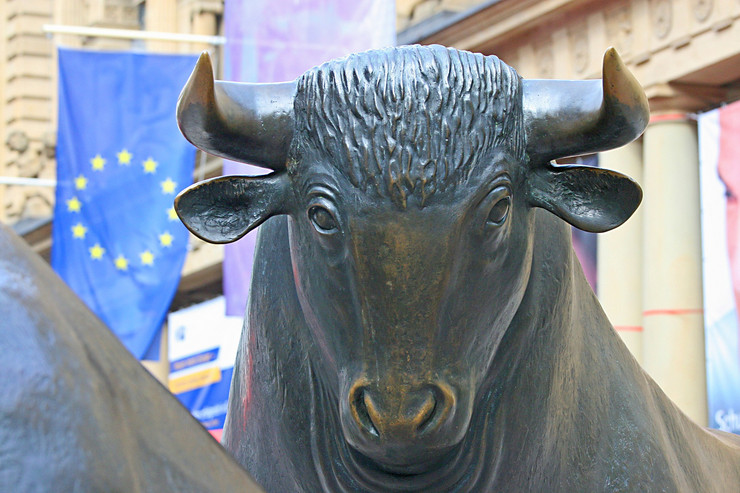 Die Statue eines Bullen. Im Hintergrund hängt die Europa-Flagge am Gebäude der Frankfurter Börse.