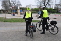 Zwei Mitarbeiter der Polizeibehörde auf Fahrrädern kontrollieren einen abgesperrten Spielplatz