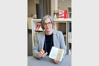 Susanne Metz sitzt vor mit Stempel und Buch in der Hand an einem Tisch.