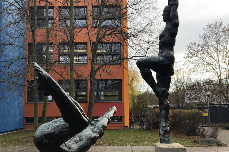 Zwei Bronzefiguren auf Betonsockeln - eine weibliche auf dem Rücken liegend mit angezogenen Beinen und über den Kopf gestreckten Armen und eine männliche auf einem bein mit hochgereckten Armen