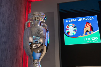 Der Pokal der UEFA EURO 2024. Im Hintergrund ist das Logo der Host City Leipzig.