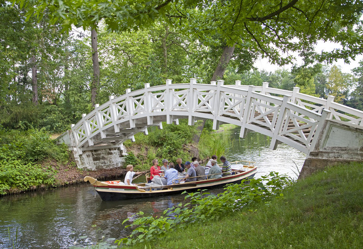Im Wörlitzer Park fahren Personen in einem Boot unter einer Füßgängerbrücke hindurch.