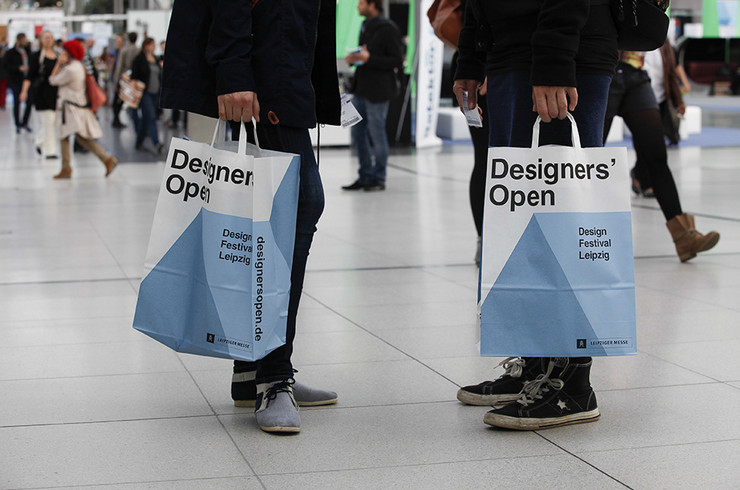 Zwei Menschen tragen Papiertüten mit Designers Open Logo