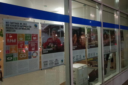 Poster mit Bildern zum Thema "fairer Handel" hängen am Schaufenster des Technischen Rathauses.