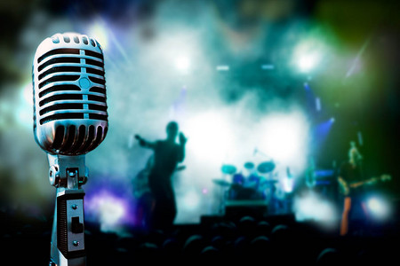 Ein Mikrofon. Im Hintergrund spielt eine Band in Konzertbeleuchtung