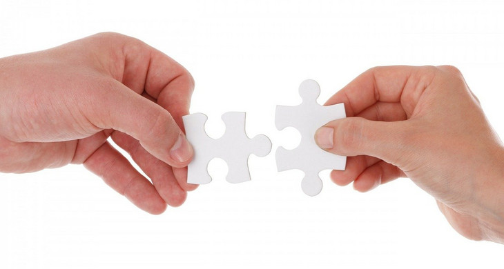 Vor einem weißen Hintergrund halten zwei Hände jeweils ein Puzzleteil. Die Teile passen ineinander.