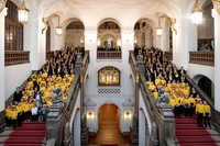 200 Kinder und Jugendliche in gelben Shirts beziehungsweise in schwarzer Kleidung mit gelbem Schal stehen auf den zwei Treppen, die vom Eingang des Neuen Rathauses zur Oberen Wandelhalle führen.