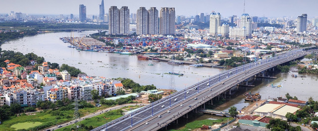Blick aus der Vogelperspektive auf einen großen Fluss, über den eine Brücke für Autos führt. Im Hintergrund sind Hochhäuser einer großen Stadt zu sehen