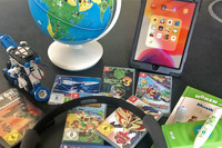 Auf eneim Tisch befinden sich ein Globus, ein Tablet-Computer, mehrere Hüllen von Computer-Spielen sowie ein Roboter