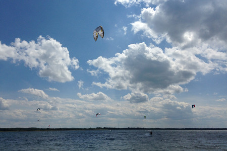 Kiteboarder auf dem Zwenkauer See. Über dem Wasser ist ein blauer Himmel mit Wolken.