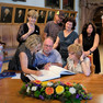 Drei Personen tragen sich an einem hölzernen Tisch mit Blumenbouqet ins Erinnerungsbuch der Stadt Leipzig ein, umringt von Angehörigen der Familie.