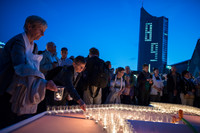 Menschen stellen auf einem Tisch auf dem Augustusplatz Kerzen ab. Im Hintergrund sieht man das Cityhochhaus mit einer erleuchtetetn 89