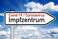 Straßenschild als Wegweiser mit Aufschrift Impfzentrum Covid-19 und Coronavirus