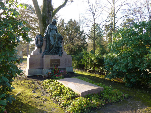 Historisches Grabmal mit einer dunklen Frauenfigur auf einem hellen Steinsockel