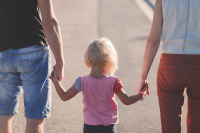 Im Mittelpunkt des Bildes sieht man ein kleines blondes Mädchen in einem rosa T-Shirt, welches die Hände seiner Eltern festhält. Die Familie läuft mit dem Rücken dem Betrachter zugewandt. 