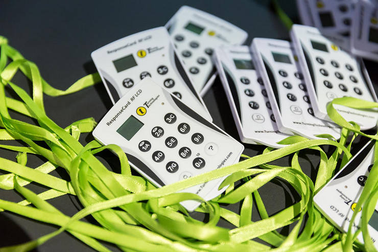 Nahaufnahme von kleinen weißen elektronischen Abstimmungsgeräten, an denen jeweils ein grünes Band befestigt ist.