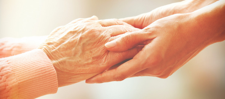 Die Hände einer älteren Person werden von einer jüngeren Person gehalten.