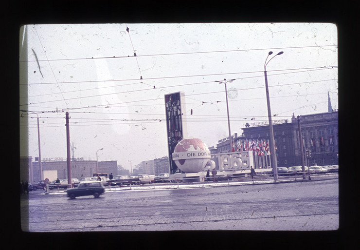 Foto aus dem 1960er Jahren mit einer Straße und einem Parkplatz auf dem Wilhelm-Leuschner-Platz sowie einer großen Weltkugel und einem Fahnenmeer als Messewerbung.