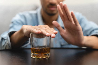 Ein Mann hält seine Hand über ein Glas Alkohol und lehnt mit der anderen Hand Alkohol ab