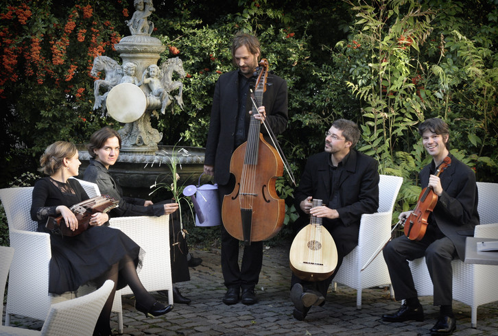 Die Musikgruppe Simkhat Hanefesh mit ihren Instrumenten in einem Garten neben einem Brunnen.
