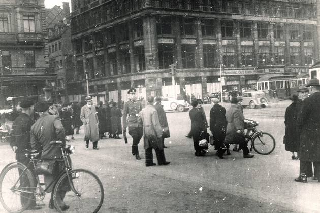 Historische Schwarz-Weiß-Aufnahme: Menschen vor einem ausgebrannten Gebäude.