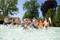 Freibadbesucher in Badesachen laufen gemeinsam in ein Wasserbecken in einem Freibad.