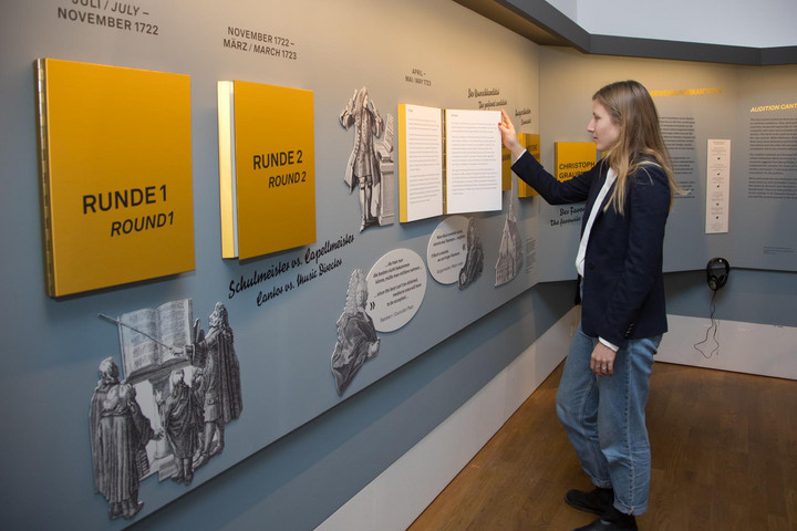 Eine Frau steht vor einer Wand mit gelben Info-Tafeln im Bachmuseum