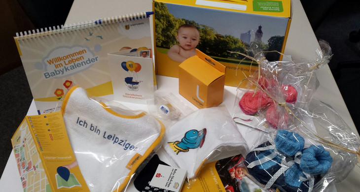 Ausgepackte Babybox mit Geschenke für Neugeborene in Leipzig. Z. B. ein Lätzchen, Schühchen, Infomaterial und ein Babykalender