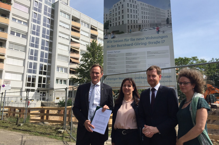 Oberbürgermeister Jung und Ministerpräsident Kretschmer stehen vor einem Schild an einer baustelle, auf dem steht "Wir bauen für Sie neue Wohnungen in der Bernhard-Göring-Straße 17". Jung hält den Fördermittelbescheid in den Händen.