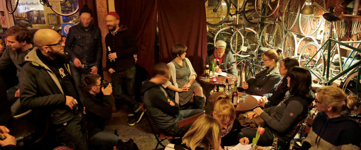 Eine kultige Bar mit vielen Fahrrädern an den Wänden. Wolf Schmid liest im Kreis von Zuhörern aus seinem Buch vor.