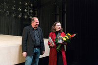 Alina-Katharin Heipe steht mit einem Blumenstrauß und einem Preis neben einer Theaterbühne