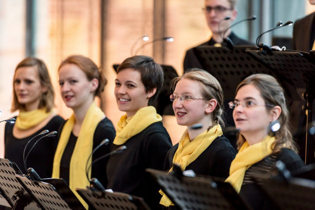 Junge Frauen mit gelbem Schal und Notenbuch in der Hand singen
