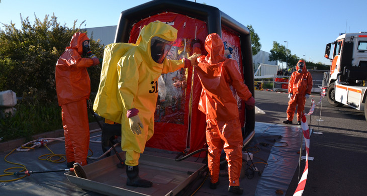 Kameraden der Freiwilligen Feuerwehr bereiten nach einem Gefahrguteinsatz einen Feuerwehrmann unter Chemikalienschutzanzug für die Dekontamination in einem speziellen Zelt vor.